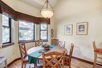 A rustic dining room with a wooden table and chairs, a chandelier, and two framed paintings on the walls.