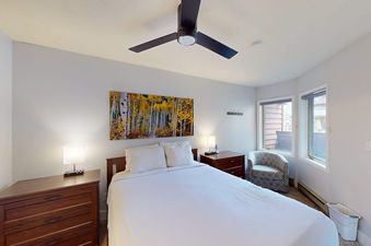A cozy bedroom in the Trappeurs Lodge 1101 with a queen bed, wooden furniture, and windows showing an exterior view.