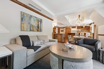 A modern and inviting living area in The Aspen 44ABC with a comfortable sofa, oval coffee table, and an armchair, blending into an open-concept kitchen and dining space.
