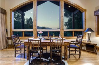 Dining area with a rustic wooden table and chairs in front of large windows at Sweetwater Jackson Hole.