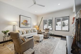 A cozy living room at The Charter B1305 with a white sofa, leather recliners, an area rug, and large windows offering views of a snowy landscape.
