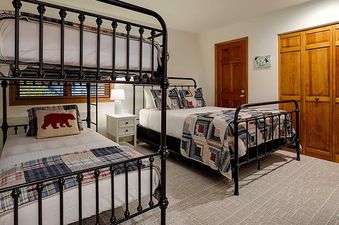 A children's bedroom at Ranch at Steamboat RA517 features black wrought iron bunk beds with patchwork quilts, a red bear pillow, a nightstand, and wooden cabinets and door.