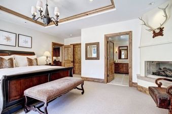 A luxurious bedroom at The Arrabelle Two Bedroom featuring a large wooden bed with leopard print pillows, a matching bench, a fireplace, and an adjoining bathroom.