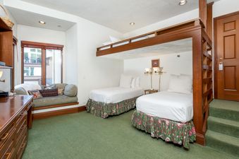 The bedroom at Plaza Lodge 2 Bedroom Silver Unit 3 features a lofted bunk bed, two twin beds below, a built-in window seat, and a green carpeted floor, all under ambient lighting.