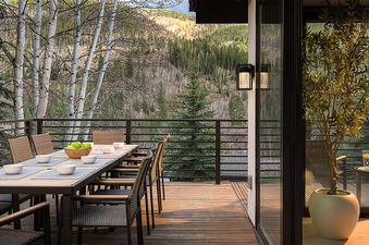 An outdoor dining deck at the Axiom Retreat with a long table and chairs, set against a backdrop of a lush mountain forest.