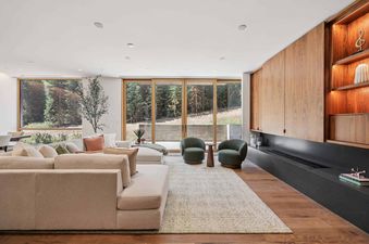 The living area at Founders Place 1403 showcases a modern design with plush seating, full-height windows offering forest views, and a stylish fireplace integrated into wooden paneling.