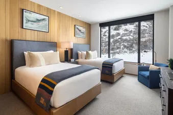 A Sylvan Lodge Double Guest Room with two beds, a large window overlooking a snowy landscape, and rustic-chic decor.