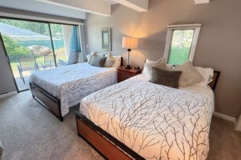A cozy bedroom with two beds, each adorned with white and brown tree-patterned bedding, and a large glass door opening to a patio.