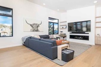 A living room with a sectional couch, a flat-screen TV, a fireplace, and a wooden shelf unit.