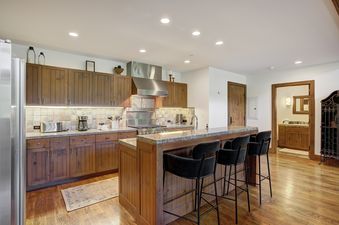 A modern kitchen at Snow Cloud Lodge 715 featuring wooden cabinetry, granite countertops, stainless steel appliances, and a breakfast bar with four black velvet stools.