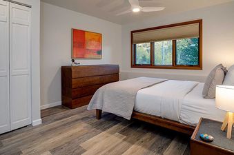 A modern bedroom in Ranch at Steamboat RA605 with a made bed, a nightstand with a lamp, a window overlooking trees, an abstract painting, and a white closet.