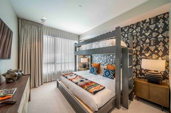 A bunk bed with vibrant bedding and pillows is positioned against a geometrically patterned wall in a bedroom.