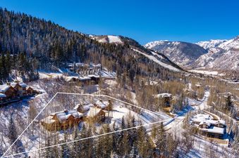 An aerial view of the Five Trees Estate in a snowy mountain landscape, featuring multiple luxury homes, dense forests, and ski slopes under a clear blue sky.