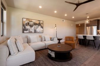 A modern and spacious living area with a white sectional sofa, a round coffee table, and an adjacent kitchen bar area.