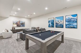 A spacious entertainment area at Frostwood Links and Lodge with a large TV, a comfortable sofa, and a modern pool table with ski resort posters.