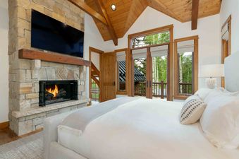 A cozy bedroom at Snow Creek Cabin features a stone fireplace and access to a private balcony.