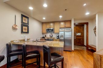 A kitchen with stainless steel appliances, wooden cabinets, and a breakfast bar with two bar stools