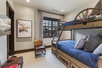 A cozy kids' bunk room at Arrowleaf Lodge 415 featuring a custom wooden bunk bed with blue bedding, a leather rocking chair, and a moose artwork.
