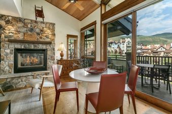 A living room with a fireplace, a large window with a view of a town in the distance, and a dining table with chairs.