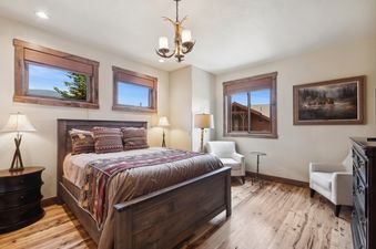 A rustic yet cozy king bedroom in Moose Jaw 34 featuring a large bed, two armchairs, and windows overlooking a natural landscape.