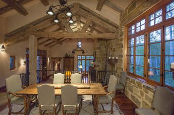 A dining room with a large wooden table and chairs, and a large window with a view of a forest.