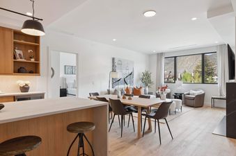 An open concept living and dining area featuring a wooden dining table with chairs, a living room with mountain views, and a partial view of the kitchen and a bedroom entrance in Frontgate 226.