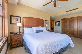 A bedroom with a king-sized bed, a leather headboard, and a ceiling fan.