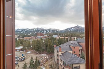 A view from a window of a building overlooking snow-capped mountains and a forest. The mountains are in the background and the forest is in the foreground.