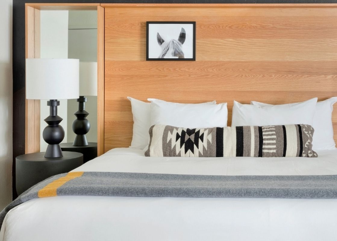 A close-up of a modern styled bed with a wood headboard and a patterned bolster pillow.