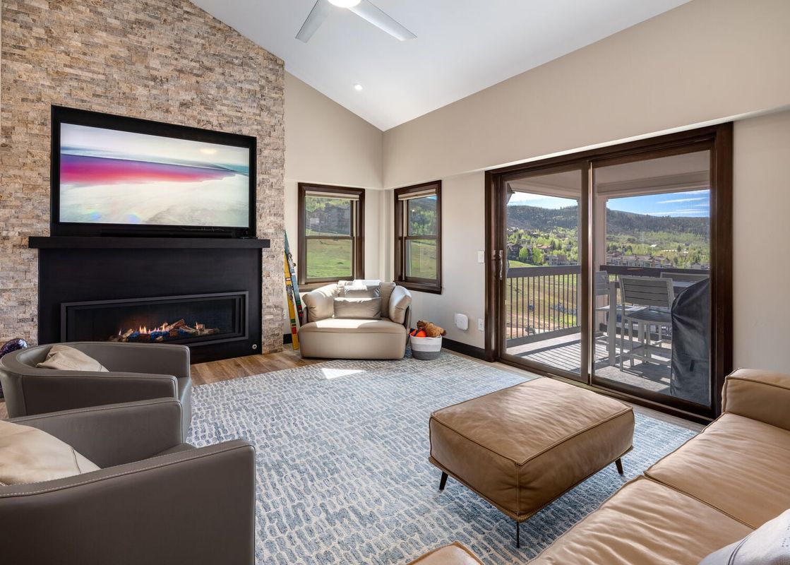 A modern and spacious living room at Torian Plum Plaza 803 featuring a stone fireplace, large TV, comfortable seating, and sliding glass doors that lead to a balcony with mountain views.