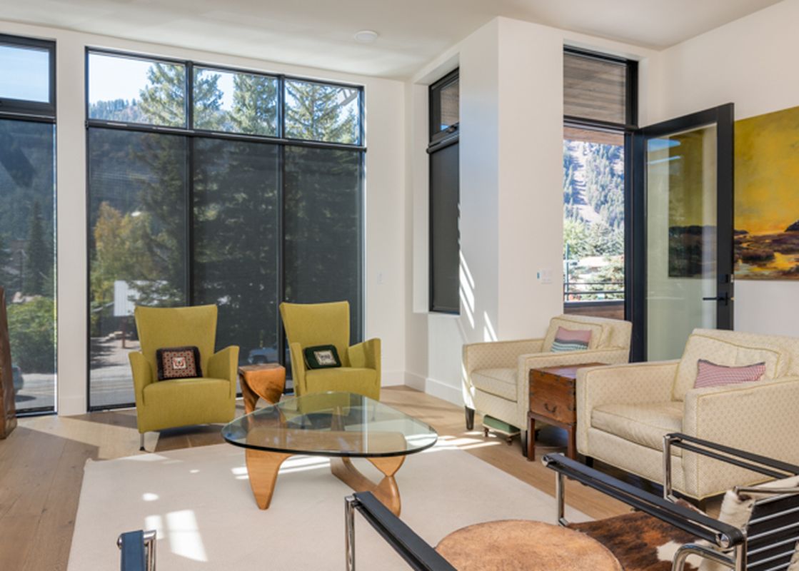 A living room with a fireplace, large windows, and comfortable furniture, including a glass coffee table.