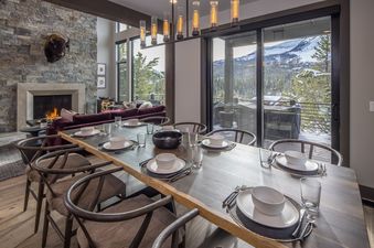 Dining area of Headwaters Hideout with a large wooden table, set for dinner, and scenic snowy mountain views through sliding glass doors.