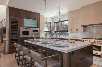 A modern kitchen with a large island set for dining, stainless steel appliances, and wood cabinetry.