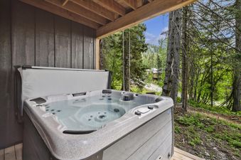 A private hot tub is set on a wooden deck, surrounded by a lush green forest with a mountain view in the background.
