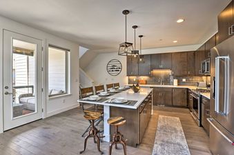 A modern kitchen with dark wood cabinets, stainless steel appliances, a large white island with seating, and light wood floors.