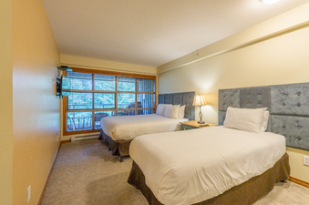 A hotel room with two beds and a large window overlooking a forest.