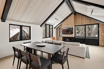 Maison Cornet open-plan living and dining area with high ceilings, fireplace, and snowy winter views.