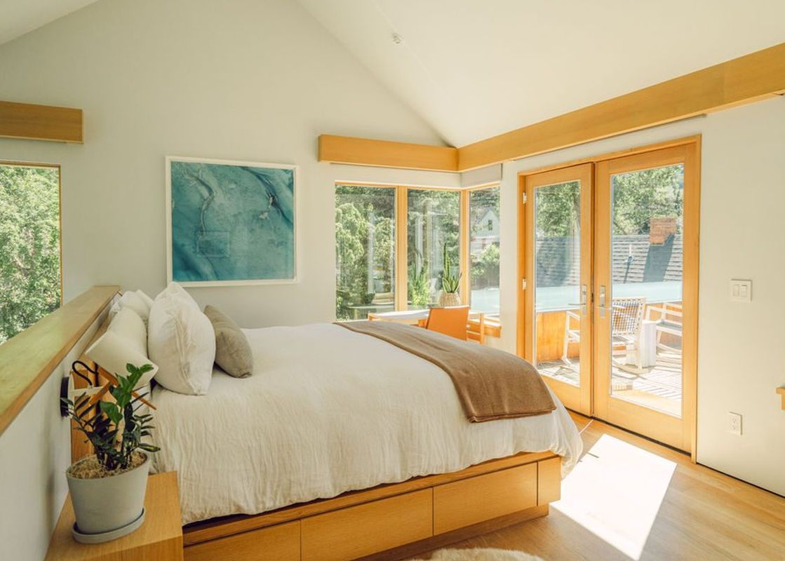 The bedroom at Silver Queen Chalet features a large bed with plush bedding, a large window with views of the surrounding forest, and a cozy armchair perfect for relaxing.