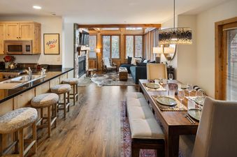 An inviting open-concept dining and living area in Portico Pines with wooden furniture and a stone fireplace.