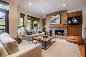 Cozy living room with a stone fireplace, gray sofas, and natural light in Ravencrest 204.