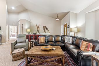 A cozy and spacious living room at Bitterroot Escape features a large dark leather sectional sofa, a wooden coffee table, and a light grey recliner, with decorative skis and snowshoes on display.