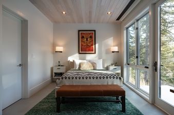 Modern bedroom with a patterned blanket on the bed, a leather bench, and large windows at West Evergreen.