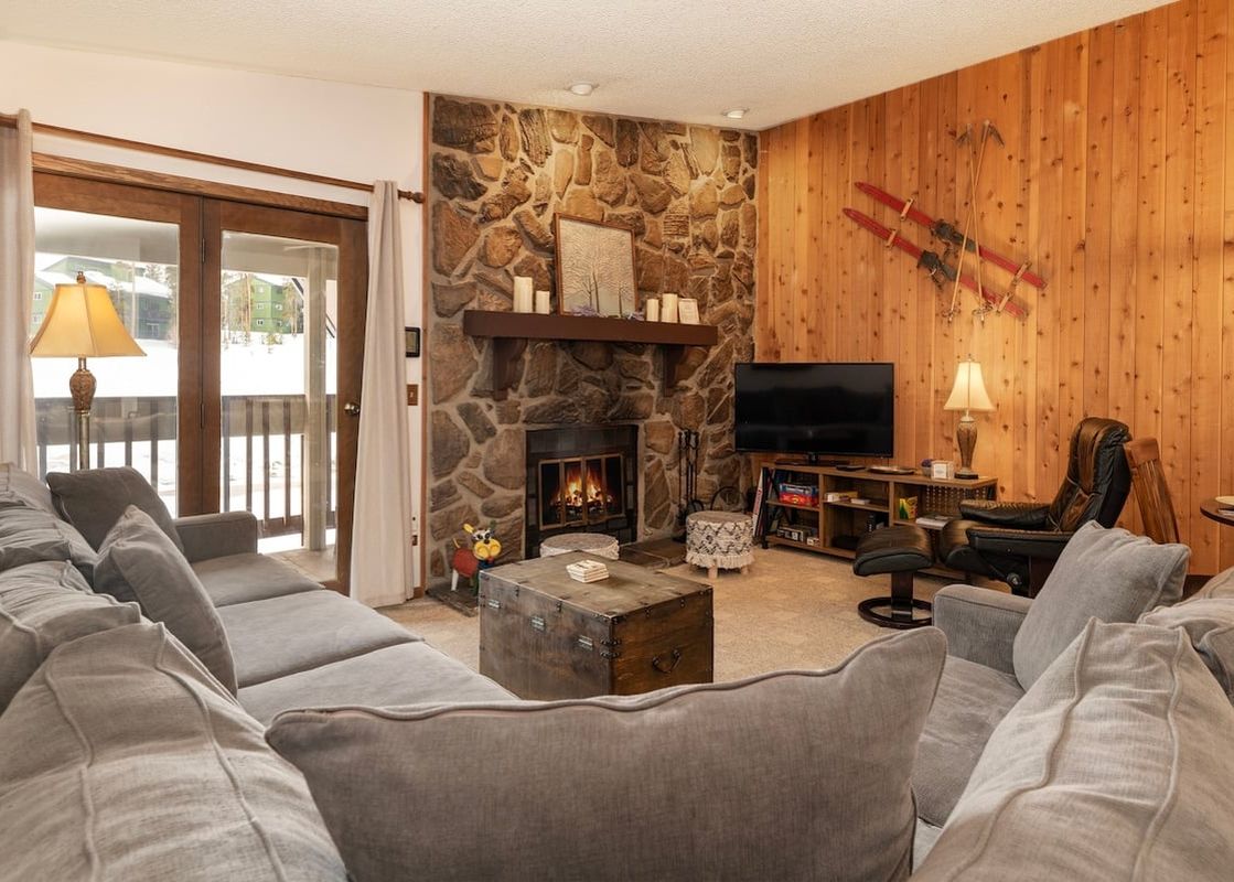 The inviting living area in Silverado II Unit 334 features a cozy fireplace, comfortable seating, and a large window offering a view of the snowy outdoors.