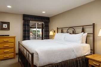 A cozy bedroom with a king-sized bed, rustic wooden furniture, and access to a private balcony at Montaneros 216.