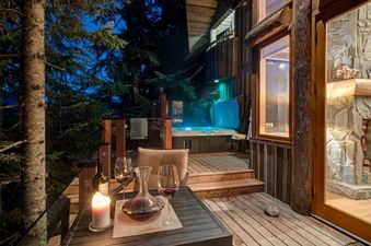 Cozy outdoor deck at Horstman 4930 with a wine setup, private hot tub, and rustic cabin exterior at night.