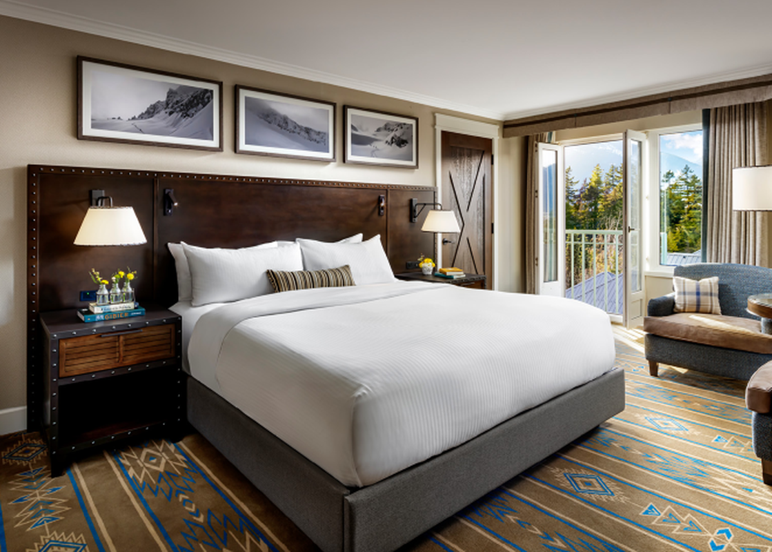 A spacious bedroom featuring a king-sized bed, stylish furnishings, and a balcony with a scenic mountain view.