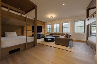 A modern bunk room and lounge area at Coeur de la Montagne with wooden bunk beds, a sectional sofa, a coffee table, and a wall-mounted TV.
