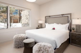 Bedroom with a king bed, white linens, grey headboard, a window with a view of the mountains, and two nightstands with lamps.