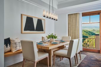 The dining area in the Peak View Two Bedroom Residence features a wooden dining table set with place settings and a decorative vase, surrounded by light-colored chairs and a built-in bench.