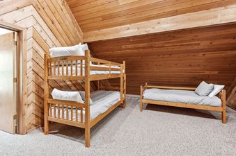 A cozy bunk room in The Village House with a wooden bunk bed, a single daybed, and warm wooden paneling on the walls and ceiling.